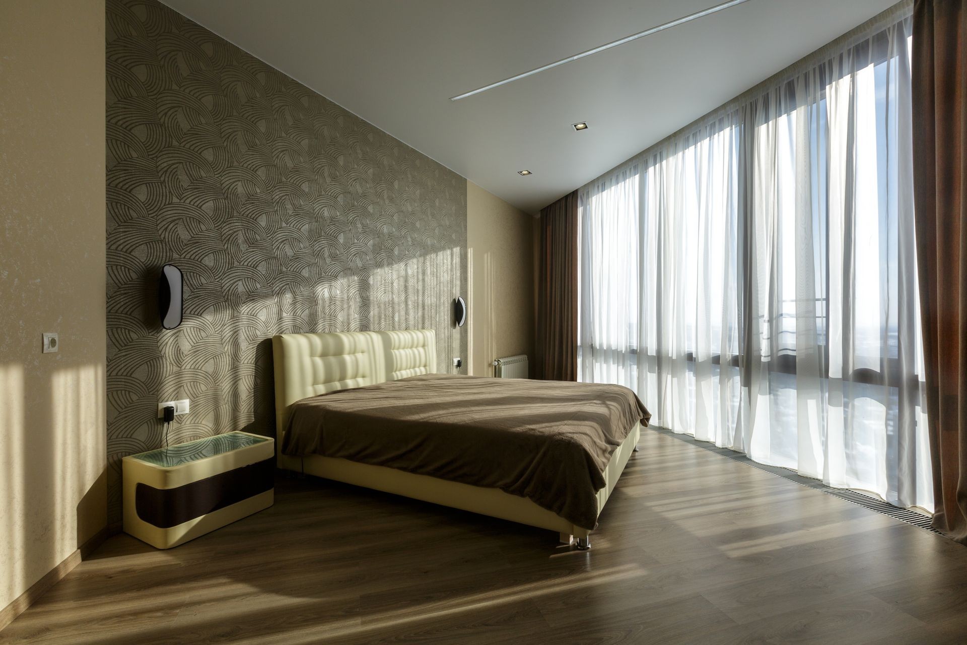 Contemporary Master bedroom In a luxurious apartment downtown. Modern designer material. Brown bed linen. Orange curtains. Big windows. Wooden floor, white ceiling. Wooden furniture.